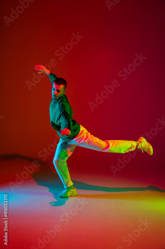 Freedom. Stylish sportive boy dancing hip-hop in stylish clothes on colorful background at dance hall in neon light. Youth culture, movement, style and fashion, action. Fashionable bright portrait.