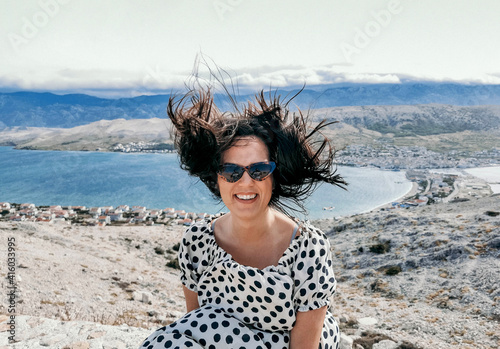 Fényképezés Smiling Caucasian woman in a polka dots flowy dress and sunglasses with hair blo
