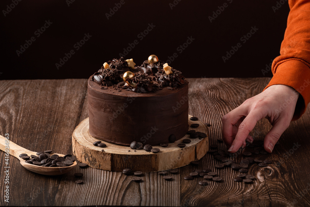 front view of chocolate cake, a hand leaving chocolate shavings, spoon wooden