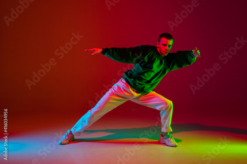 Style. Stylish sportive boy dancing hip-hop in stylish clothes on colorful background at dance hall in neon light. Youth culture, movement, style and fashion, action. Fashionable bright portrait.