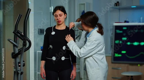 Scientist researcher preparing woman patient for endurance test attaching electrodes on professional body equipment. Team of doctors monitoring health of patinet, vo2, ekg scan runs on computer screen photo