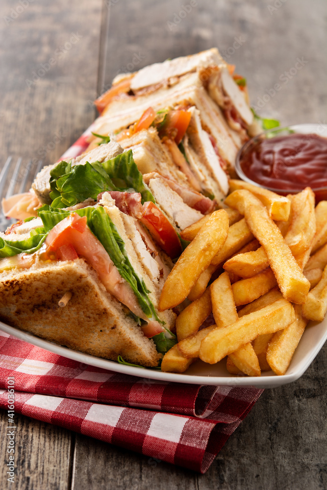Club sandwich and French fries with ketchup sauce on wooden table