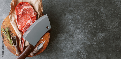 Tableau sur toile on a wooden block for meat a fresh raw tamahawk steak or a cowboy steak with a butcher's chopping ax for meat, next to it is a mixture of peppers and coarse salt, milled with thyme