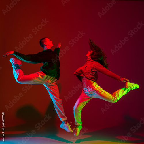 Flying. Stylish sportive couple dancing hip-hop in stylish clothes on colorful background at dance hall in neon light. Youth culture, movement, style and fashion, action. Fashionable bright portrait.