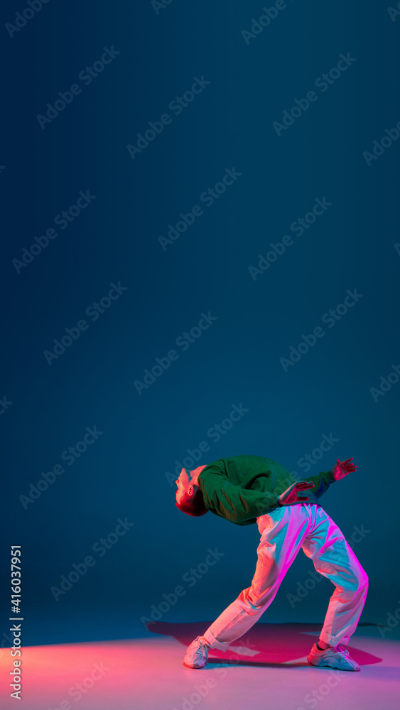 Flyer. Stylish sportive boy dancing hip-hop in stylish clothes on colorful background at dance hall in neon light. Youth culture, movement, style and fashion, action. Fashionable bright portrait.