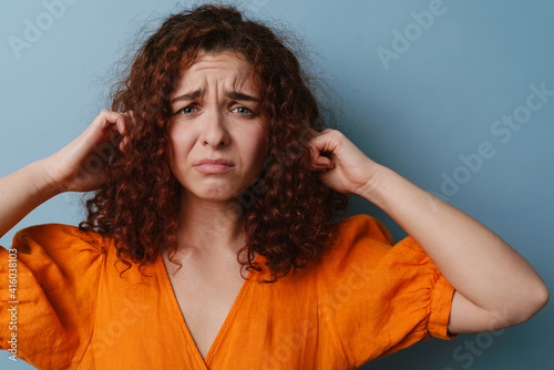 Unhappy ginger woman grimacing and plugging her ears