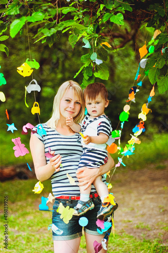 Happy family and holiday concept. Little boy in a sailor suit sitting on mother hands and laughing on a summer sunny day. paper decorations on tree for children's birthday close up.