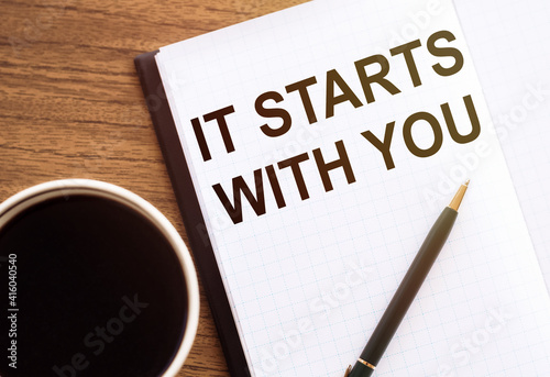 IT STARTS WITH YOU - text on notepad on wooden desk.