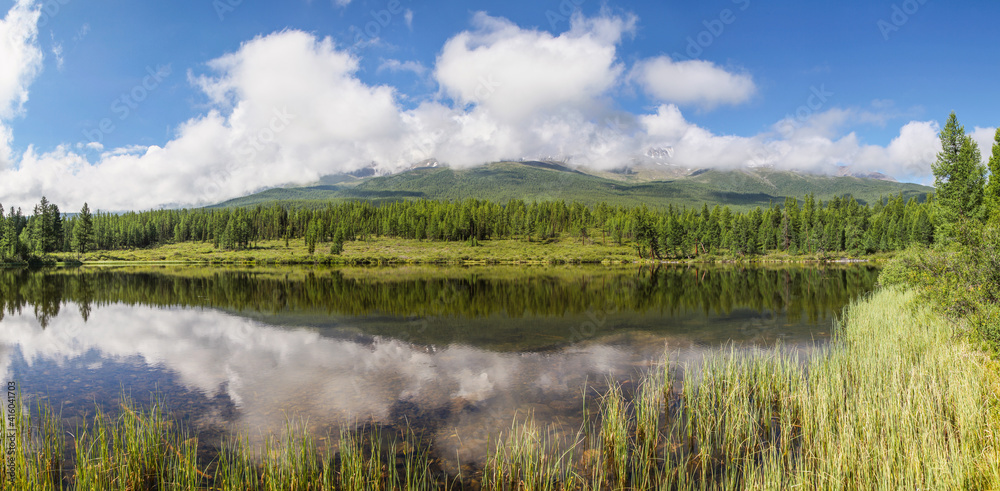 Forest lake on a quiet summer morning, clouds over mountain peaks