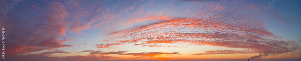 intense dramatic panoramic sunset with cirrus clouds illuminated by red sunbeams