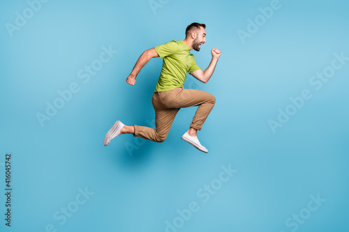 Full size photo of excited man run sale jump up wear brown pants hurry isolated on pastel blue color background