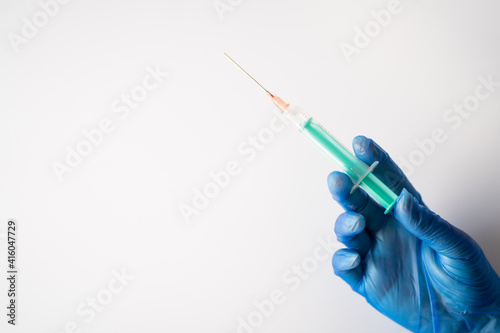 A nurse wearing blue gloves, holding a vial of coronavirus vaccine with one hand, and with the other a needle, with a white background