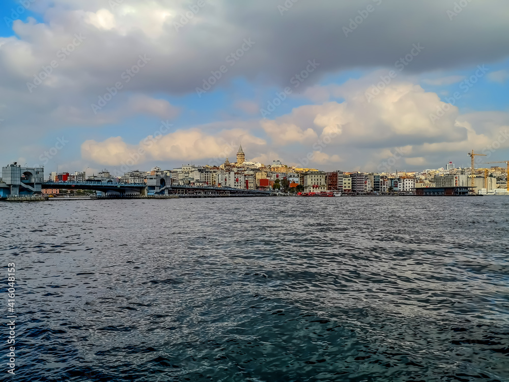 Sea panorama of Istanbul (Turkey) with Galata tower among city buildings on a cloudy summer-autumn day. The Bosphorus coastline with dark blue-gray water