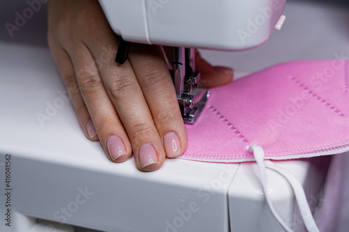 A woman sews a protective pink face mask 