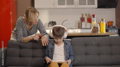 The little boy who playing games very much with his headset from the pad, His mother comes shouting behind him, take off his headphone and gets angry at him. Technology addiction concept. Slow motion