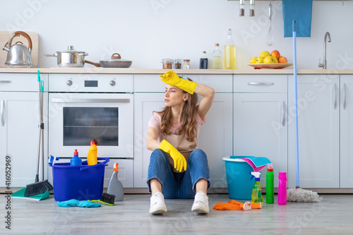 Young housewife tired from domestic work sitting on kitchen floor, wiping her forehead photo