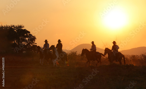 The silhouette of  rider as cowboy outfit costume with a horses and a gun held in the hand against smoke and sunset background