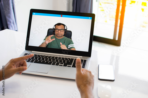 A man wearing headphones is using a laptop to communicate via video conferencing. Conversation during the coronavirus or COVID 19 vent. Work at home via the Internet. Concept social distance.