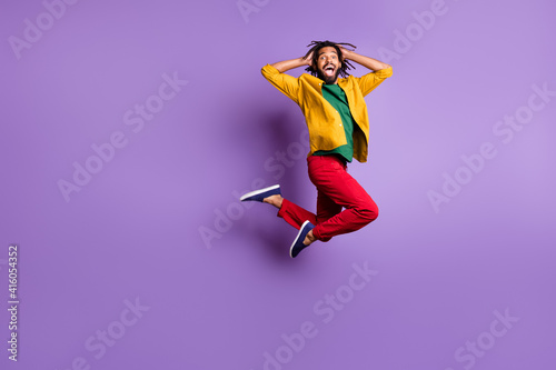 Full length photo of impressed dark skin man wear yellow shirt jumping high arms head isolated violet color background