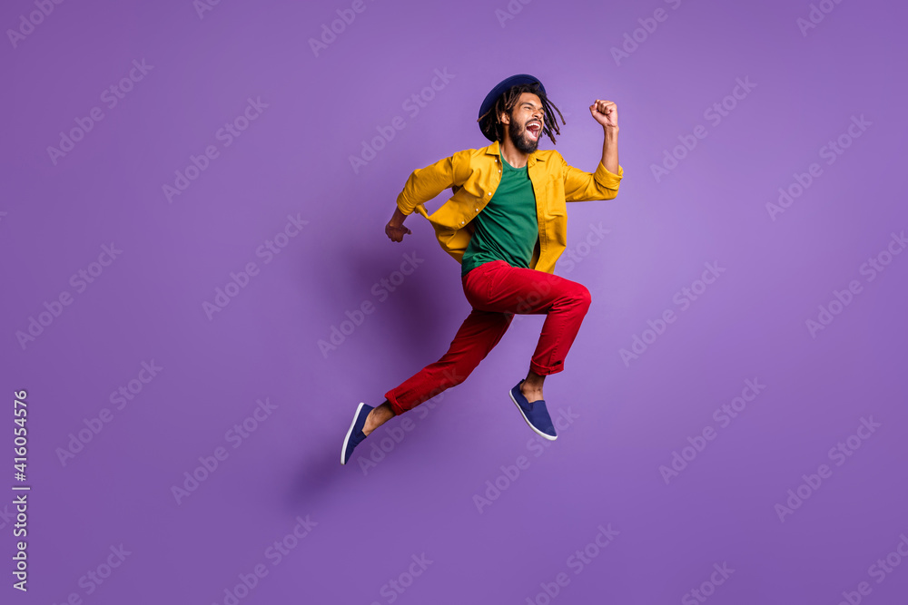 Full length photo of funky dark skin guy dressed yellow shirt headwear jumping running fast isolated purple color background