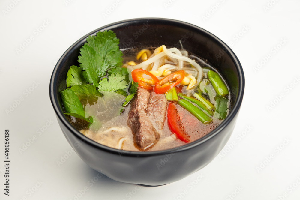 Asian soup with beef and Udon noodles in a black karelian. Ingredients broth, beef, bell pepper, Udon noodles, soy sprouts, miso paste, soy sauce, green onions, vegetable oil, For restaurant menu