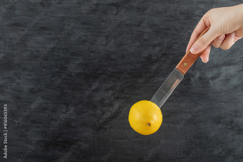 Hand holding a knife with a whole lemon Hand holding a knife with a whole lemon