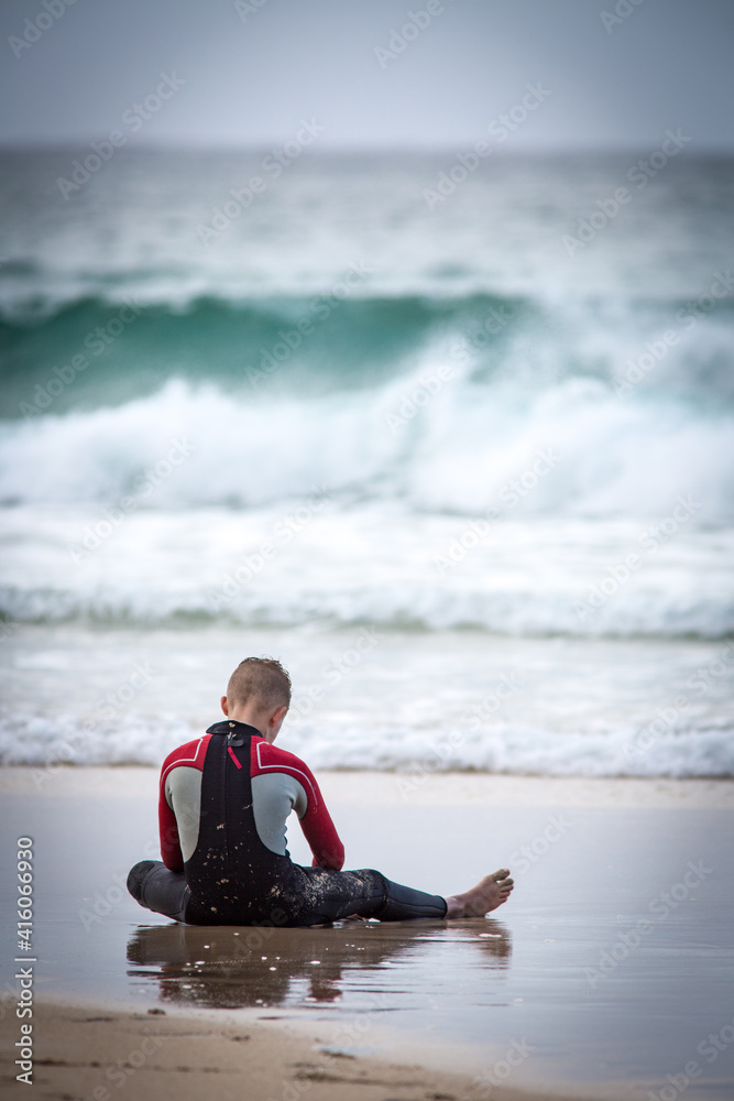 person sitting on the beach in a wetsuit