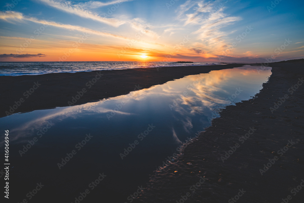 波の水たまりに反射した夕日と空と雲