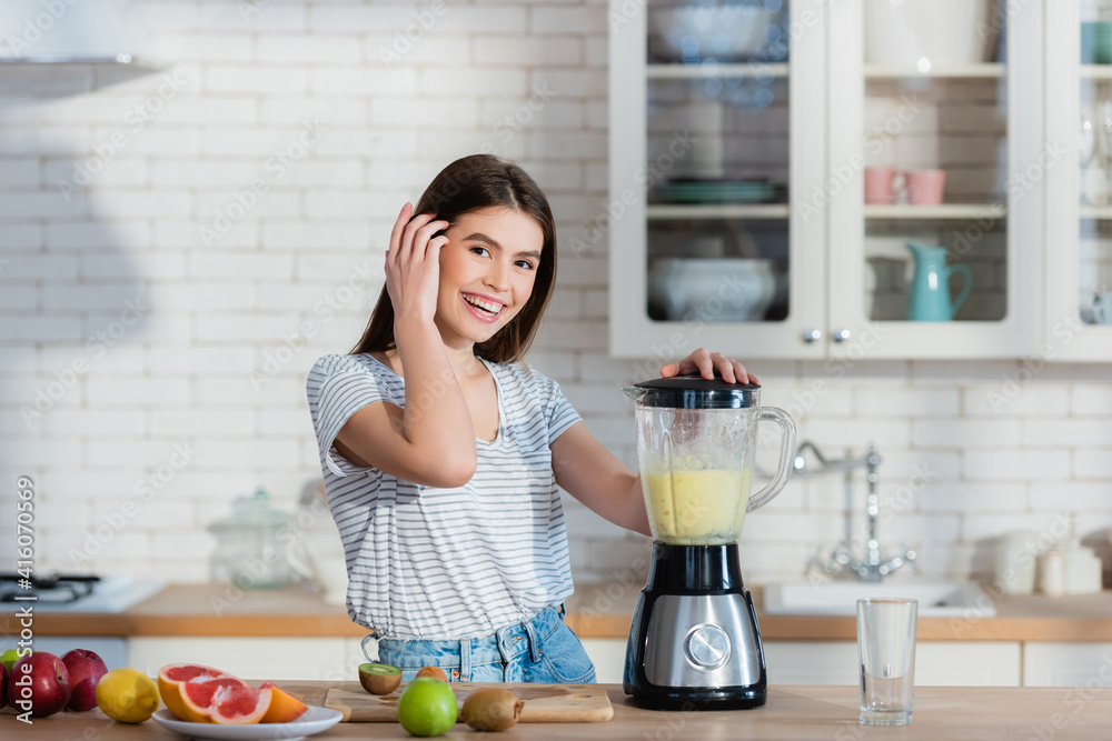 happy woman looking at camera while preparing fruit smoothie in blender
