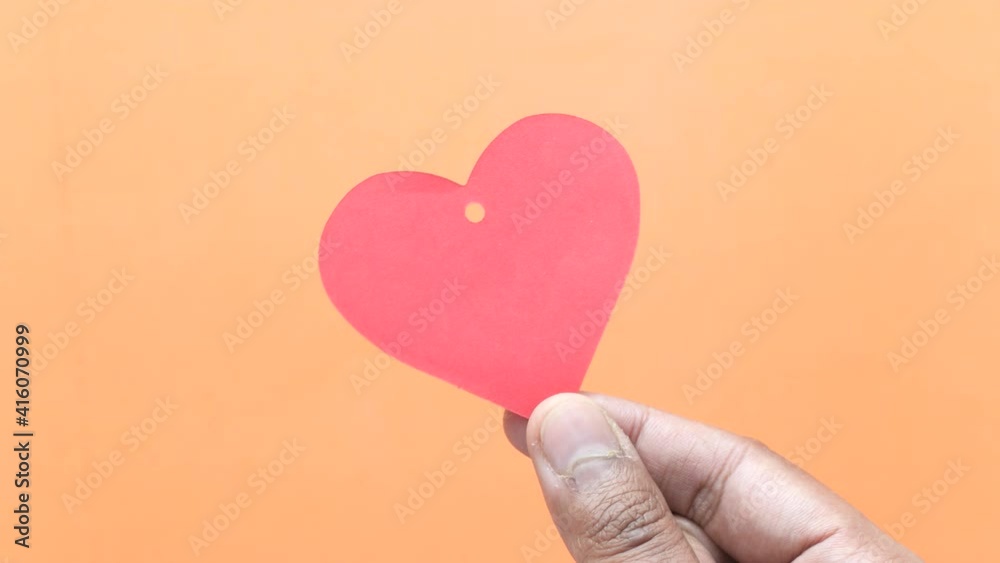 Close up of person hand holding red heart symbol on orange background Close up of person hand holding red heart symbol on orange background