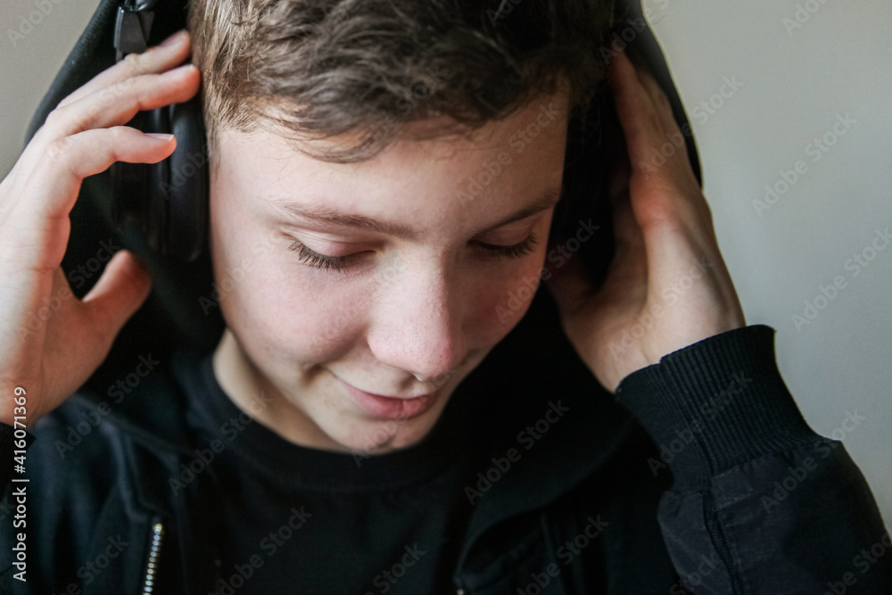 Fototapeta premium A teenage boy in a black hood and large headphones listens to music with his eyes closed