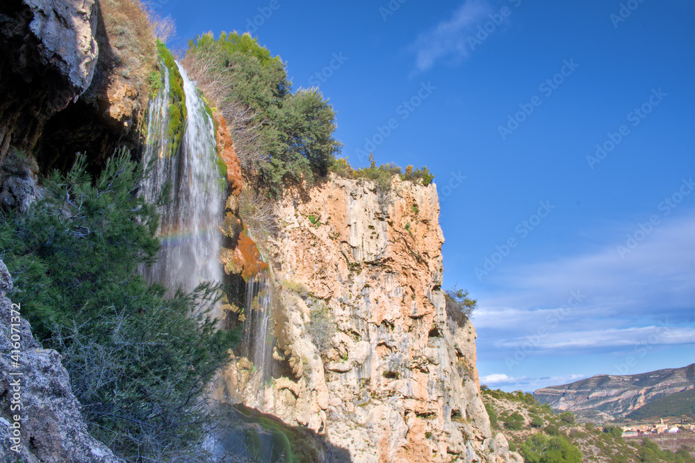 A large beautiful waterfall in a forest with blue water and trees.