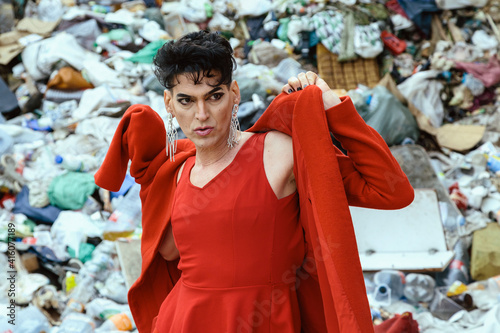 Foto Transgender woman in red clothing, putting on your coat, with a landfill garbage background
