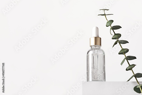 Natural skin care products concept. Herbal mineral cosmetics, serum, hyaluronic acid on white podium. Transparent dark glass bottle with dropper, copy space photo