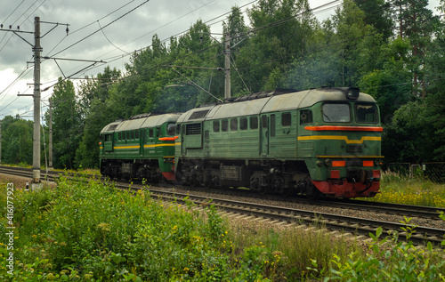 An old green locomotive rides on the railway near the forest