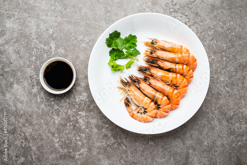 A plate of boiled black tiger prawns and seasoning sauce on cement shading