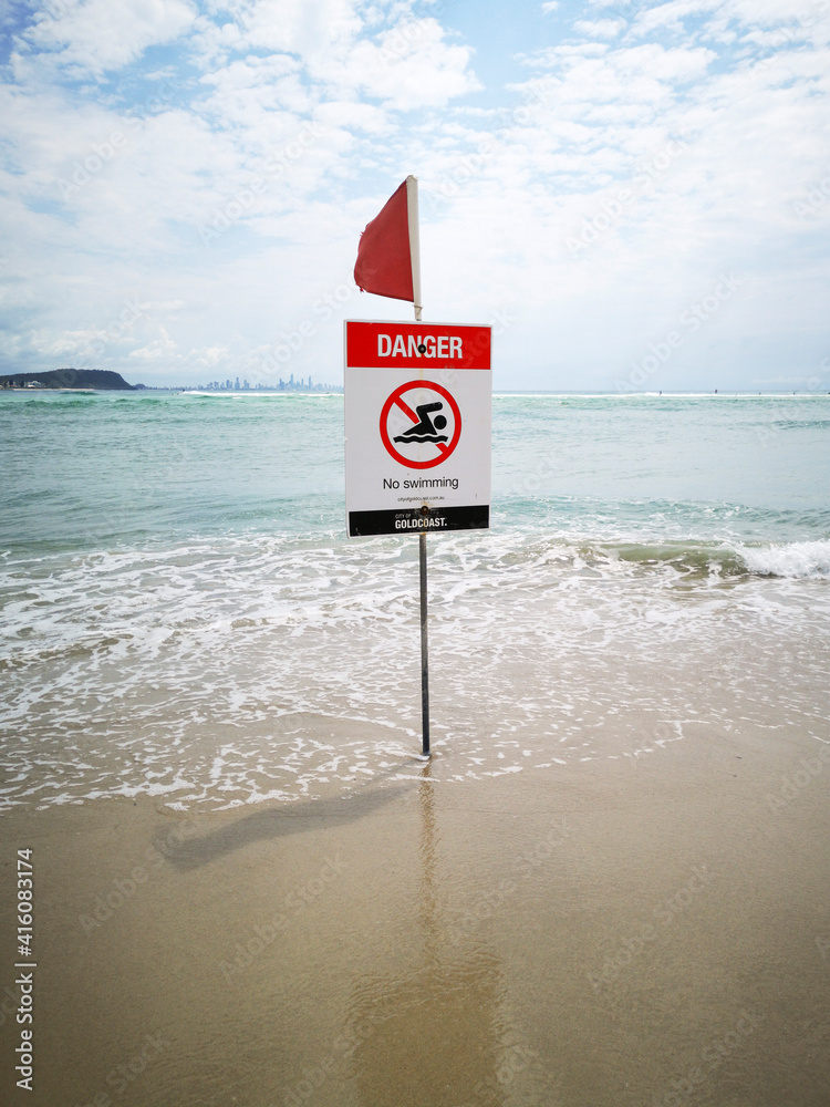Danger No Swimming information sign with a red flag near the ocean in ...