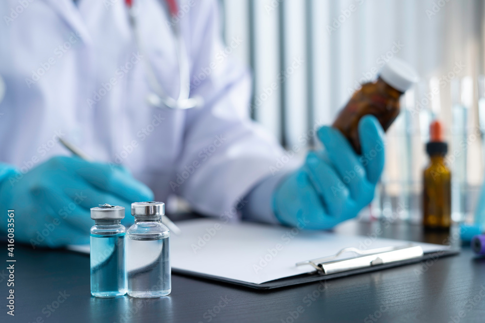 A doctor or pharmacist sits at a desk, holds or shows a bottle of medicine in his hand and writes a prescription explaining its properties. Concept of medical treatment, pharmacy or health insurance A doctor or pharmacist sits at a desk, holds or shows a bottle of medicine in his hand and writes a prescription explaining its properties. Concept of medical treatment, pharmacy or health insurance