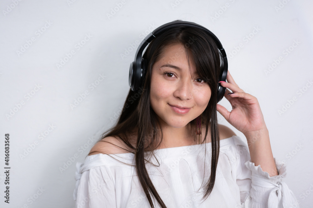 beautiful smiling hispanic woman with long black hair wearing a black wireless headset with her hands gripping the headphones, isolated in white background beautiful smiling hispanic woman with long black hair wearing a black wireless headset with her hands gripping the headphones, isolated in white background