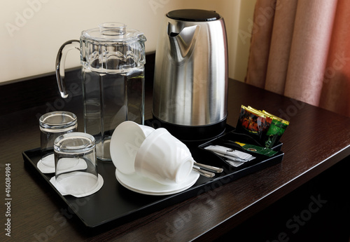 A set of dishes on a black tray for tea and coffee. Teapot, glass jug, glass glasses, cups. The table is dark wooden.