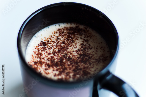 Black cup of aromatic coffee with froth and chocolate chips. Delicious creamy foam. White bright minimalistic background