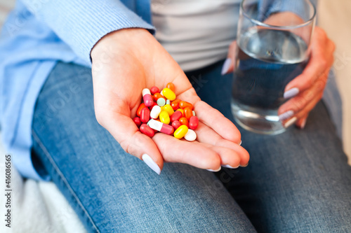 Woman holds multicolored pills and glass of water in hands. Taking supplements or antibiotic, vitamins, antidepressant, painkiller medication. Close-up.