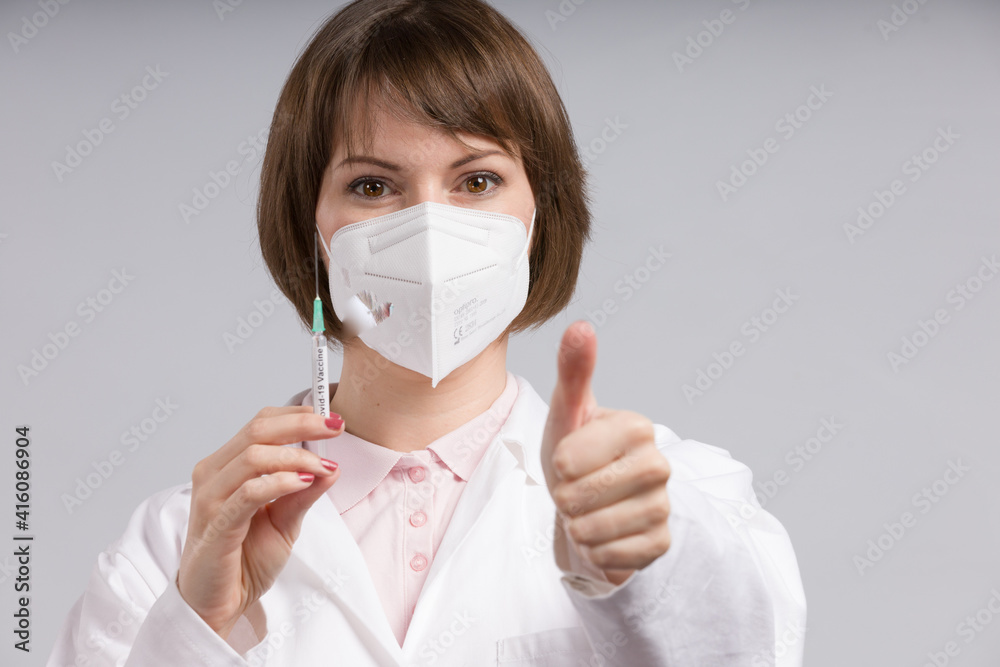 female doctor or nurse with syringe pulled up with a vaccination serum shows thumbs up female doctor or nurse with syringe pulled up with a vaccination serum shows thumbs up