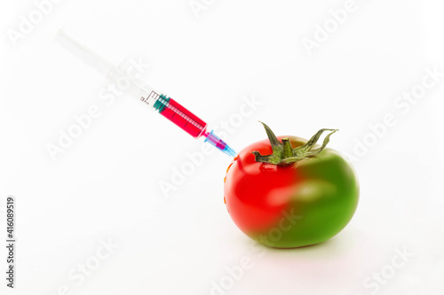 Tomato and syringe with nitrates isolated on a white background. Pesticides and nitrates are injected into tomato with a syringe. GMO food ingredient concept. Green tomato turns red
