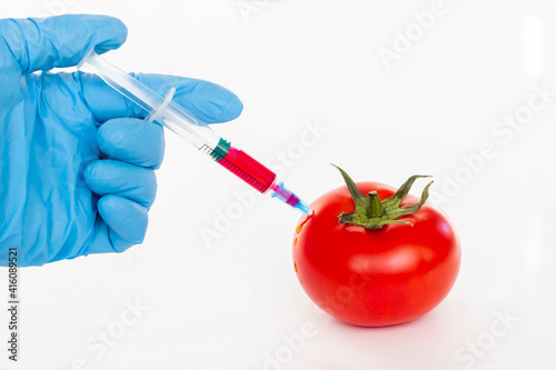 Red tomato and syringe with nitrates isolated on a white background. Pesticides and nitrates are injected by a scientific worker into a red tomato with a syringe. GMO food ingredient concept