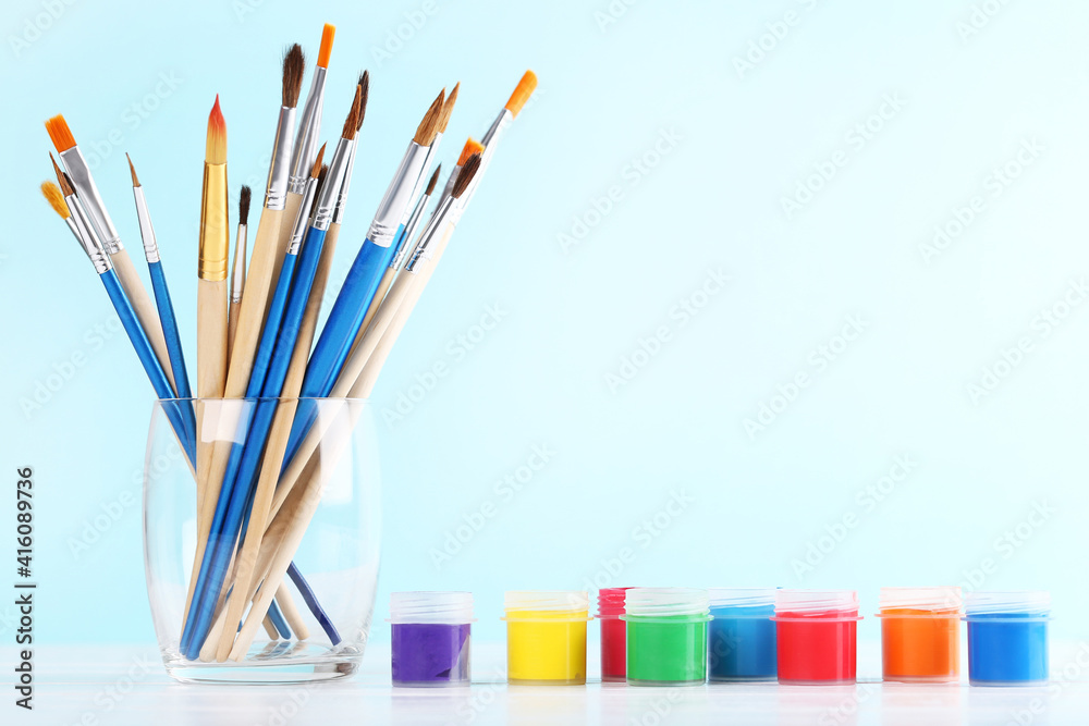 Obraz premium Artistic brushes in glass and colorful gouache paints on blue background