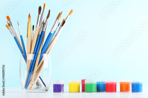 Artistic brushes in glass and colorful gouache paints on blue background