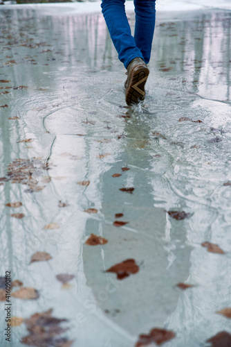 Boy teenager in boots jumps, runs through the puddles in the cold autumn