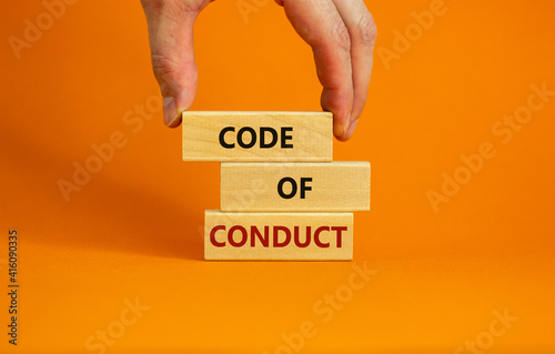 Code of conduct symbol. Concept words 'Code of conduct' on wooden blocks on a beautiful orange background. Businessman hand. Business and code of conduct concept. Copy space.