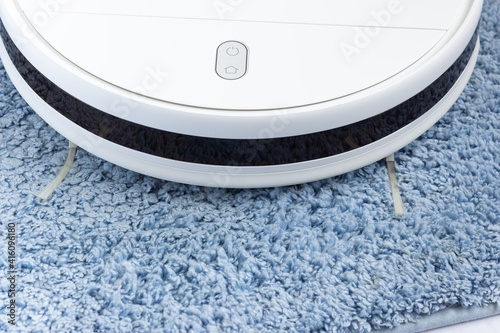 Part of a white robot vacuum cleaner on a blue carpet, side view. Home cleaning, technology, smart home